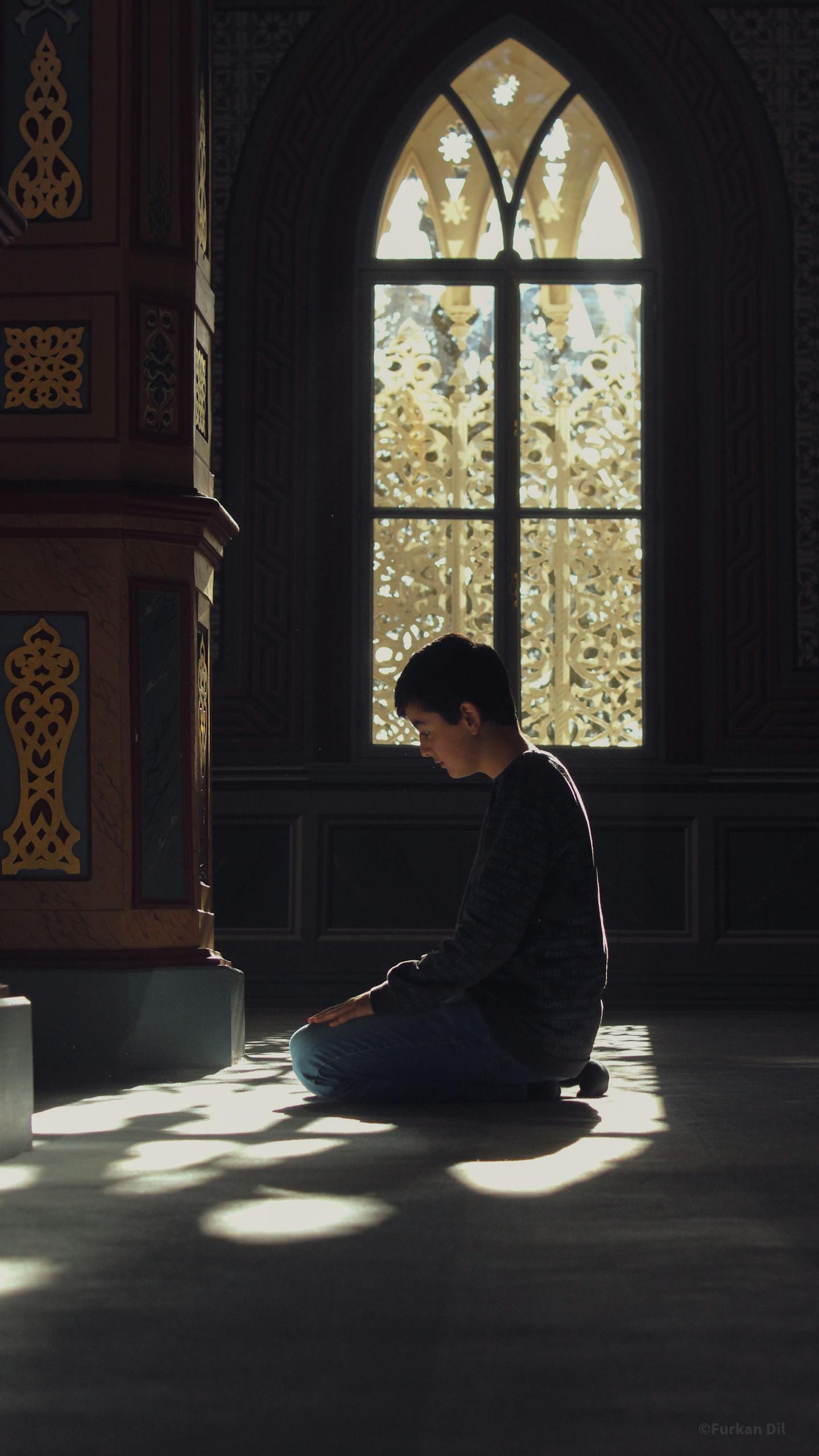 A child kneeling and praying inside a beautifully lit mosque interior, highlighting spirituality and peace.